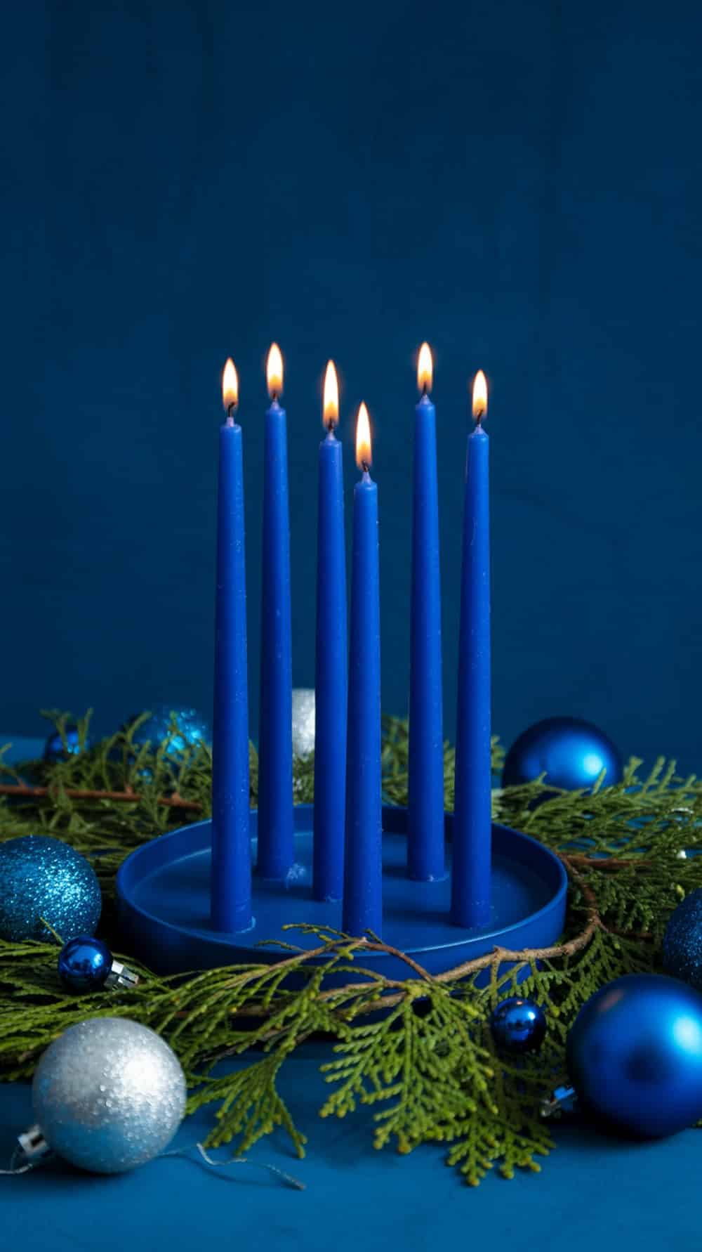 A display of cobalt blue candles with a circular holder, surrounded by blue and silver ornaments and greenery.