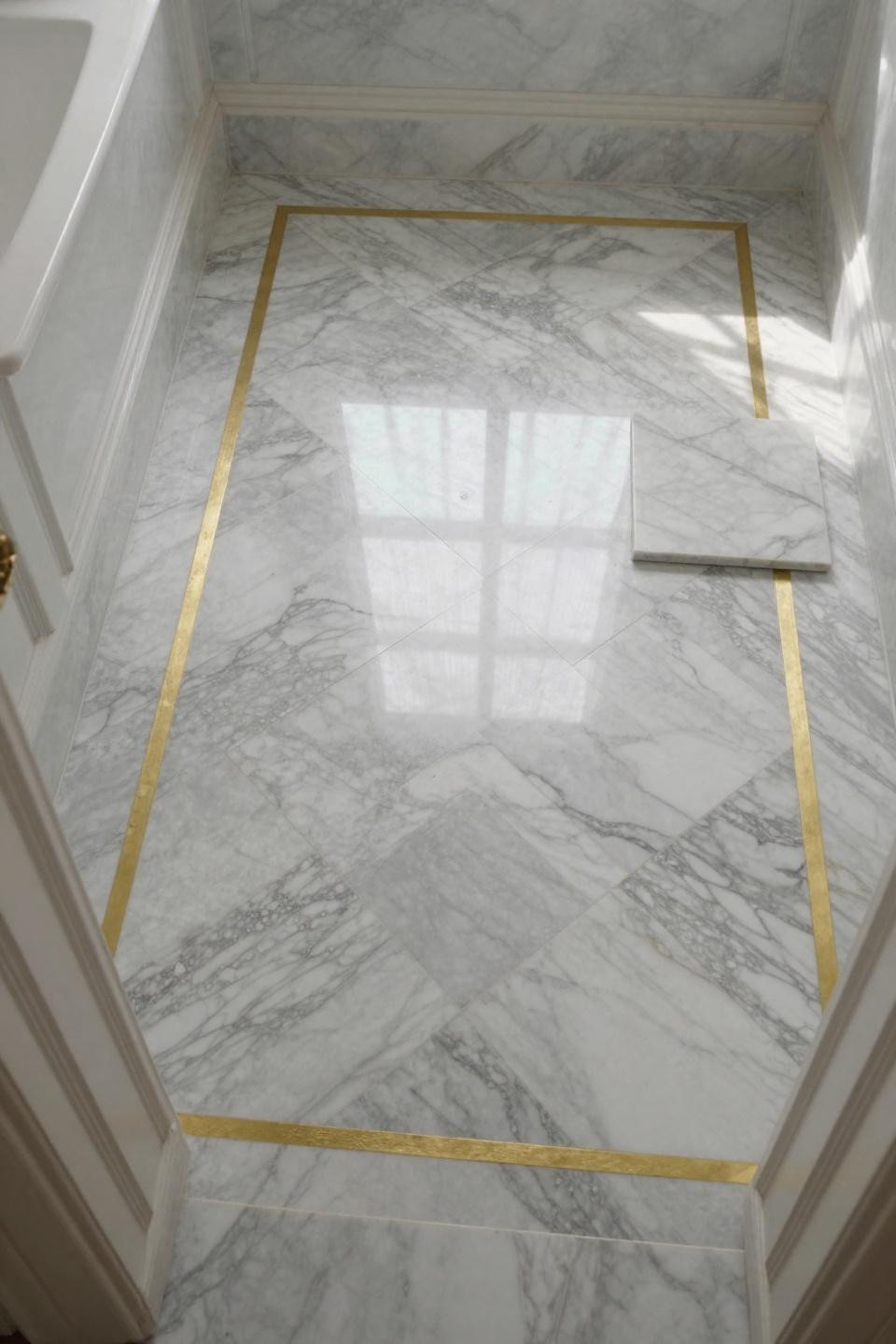 bathroom flooring ideas showing calacatta marble chevron pattern with dramatic gold veining and brass inlay from doorway view