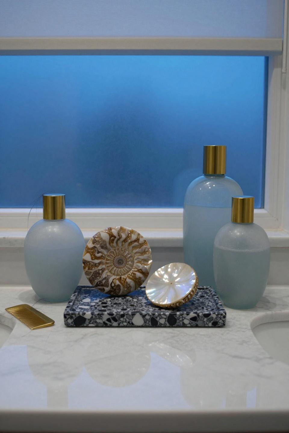 carrara marble counter with ammonite fossil glacier-blue glass vessels brushed brass accessories and terrazzo tray